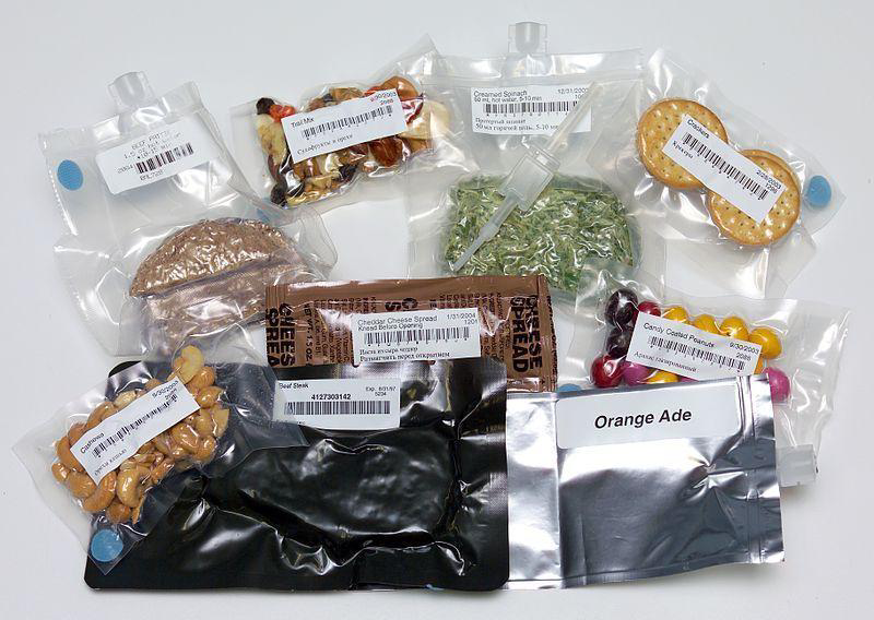 A collection of packaged space food items including nuts, crackers, cheese spread, and a drink packet labeled 'Orange Ade'.