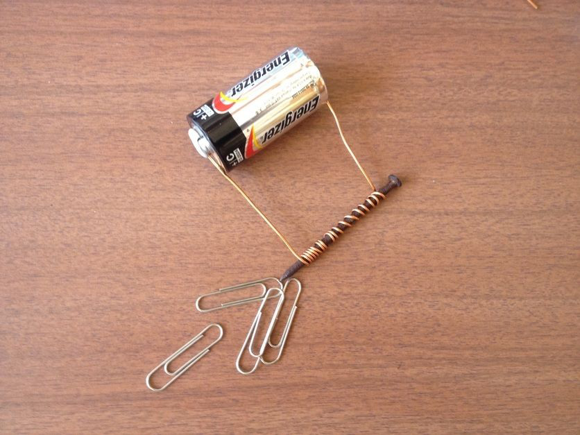 Battery, wire coil on nail, and paper clips demonstrating an electromagnet