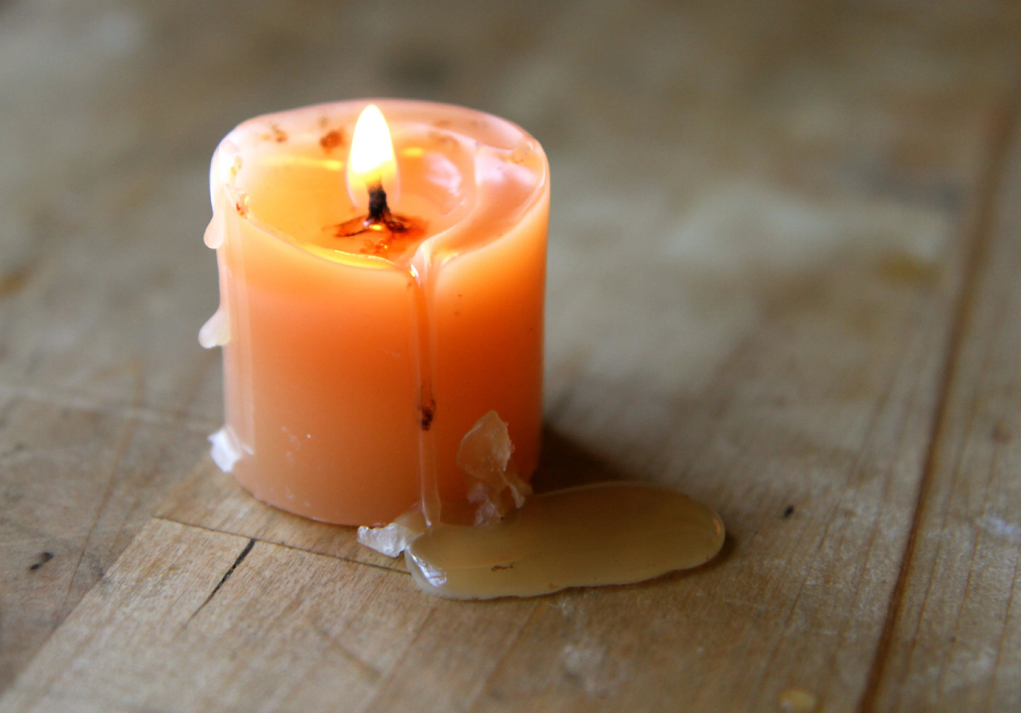 Burning candle with melted wax on a wooden surface.
