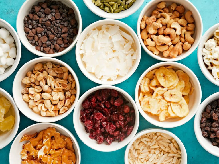 Bowls containing different trail mix ingredients such as nuts, dried fruit, and chocolate chips.