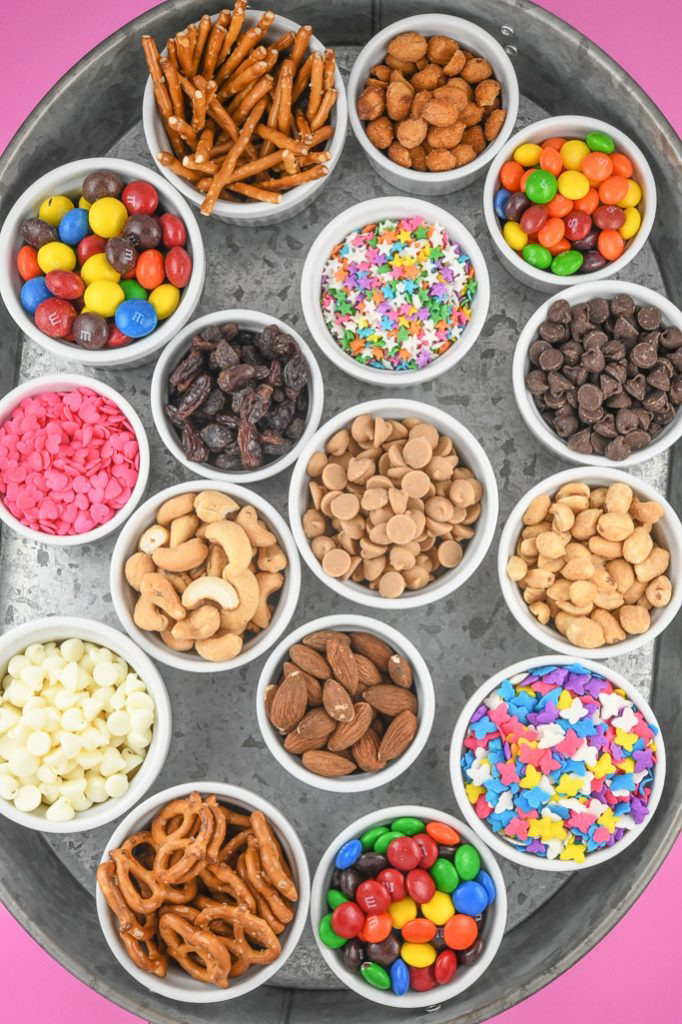Tray with many small bowls of trail mix ingredients including nuts, pretzels, candies, and sprinkles.