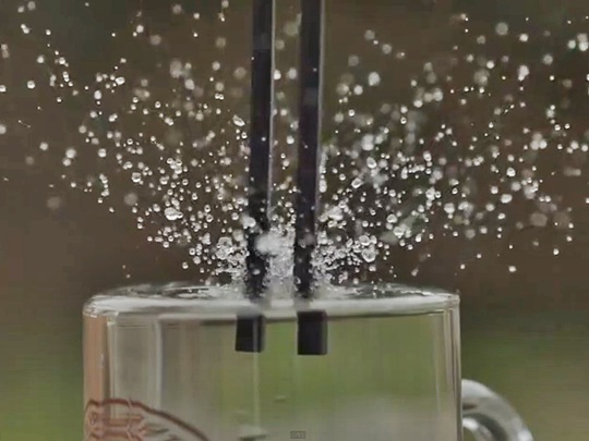 Water droplets splashing around tuning forks vibrating in a glass of water