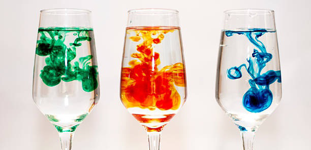 Three glasses of water with green, orange, and blue food coloring spreading in the water.