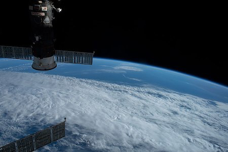 A satellite orbiting Earth above clouds and the curved horizon.